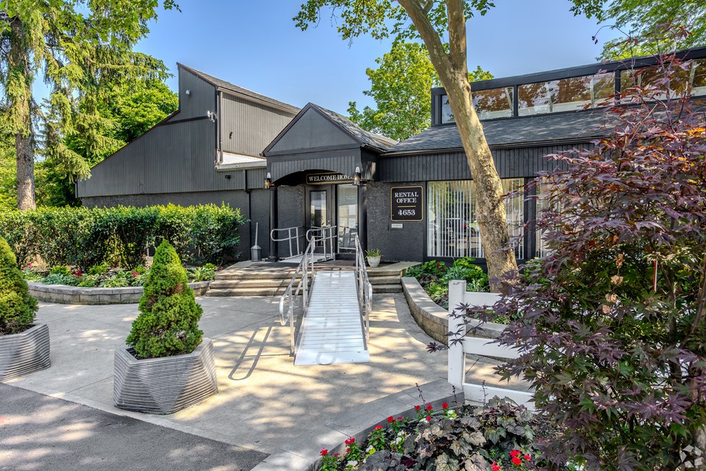 A building with a dark grey exterior and a black roof is surrounded by a well-manicured garden with a variety of plants and trees. at Commons At Waters Edge, Columbus Ohio