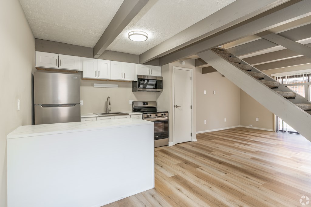 A kitchen with wooden floors and a staircase leading to the upper floor.