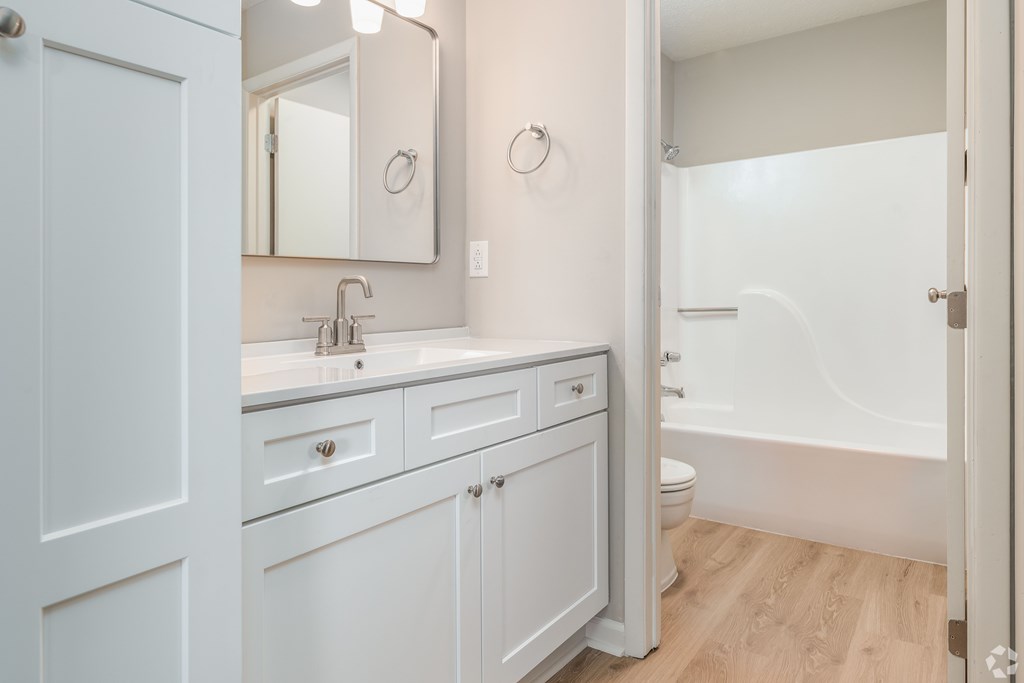 A white bathroom with a sink, mirror, toilet and bathtub.
