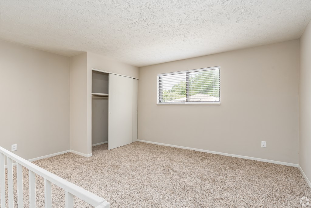 A room with a carpeted floor and a window with blinds.