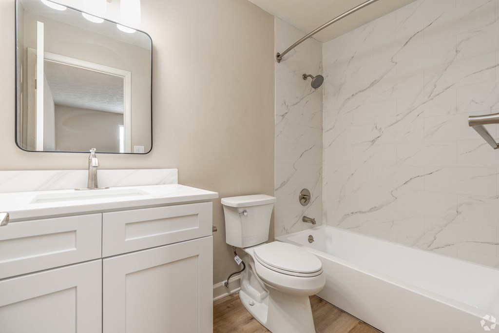 A white bathroom with a marble wall and a large mirror.