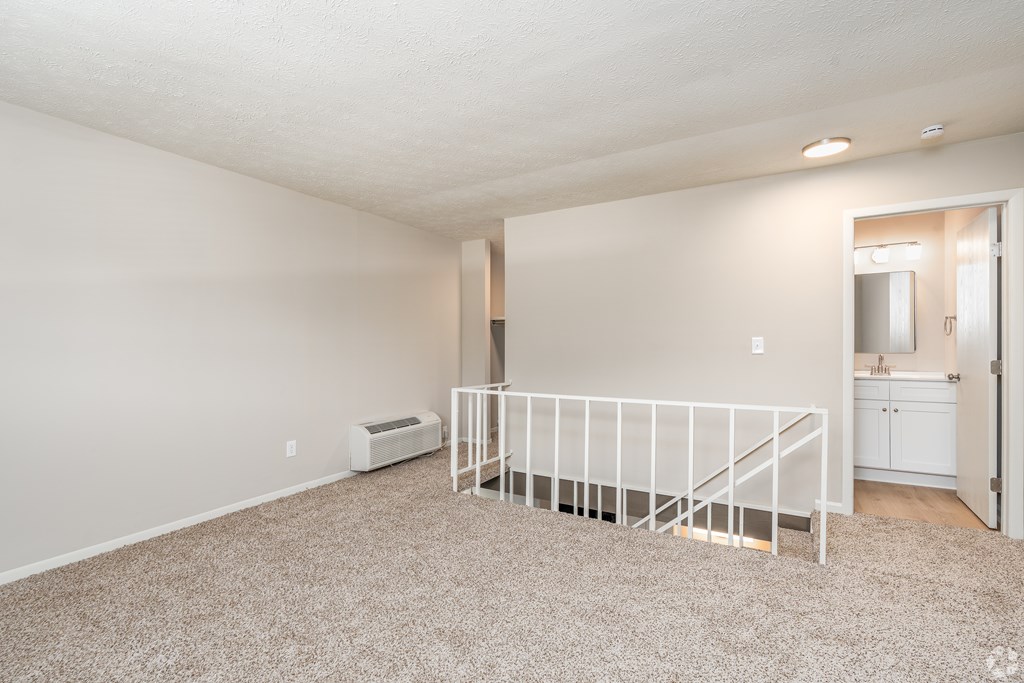 A white room with a carpeted floor and a white railing.