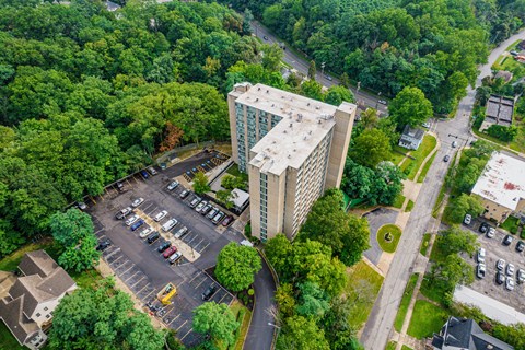 A tall building is surrounded by a parking lot and trees.