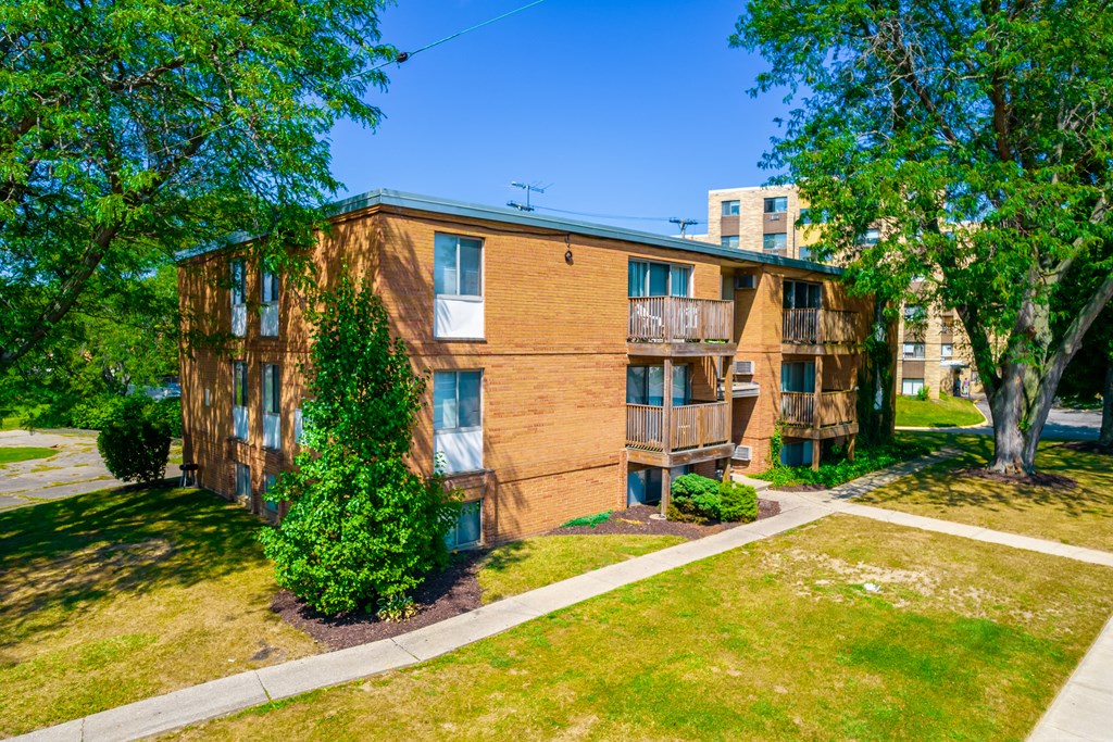exterior view of a brick apartment building with green grass and trees