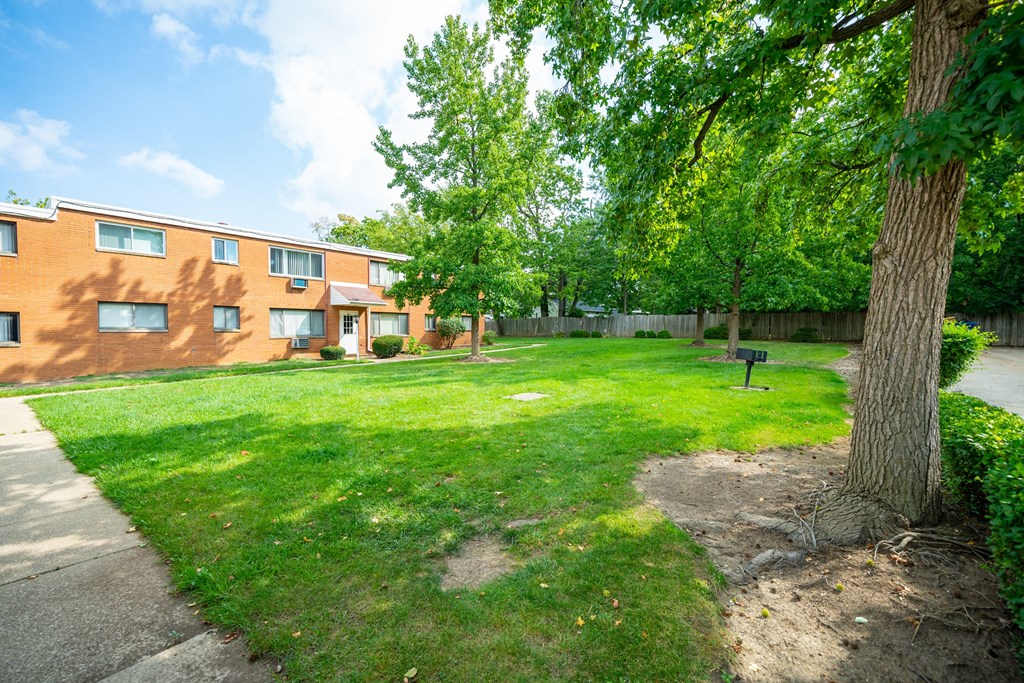 the backyard of a brick apartment building with a lawn and trees