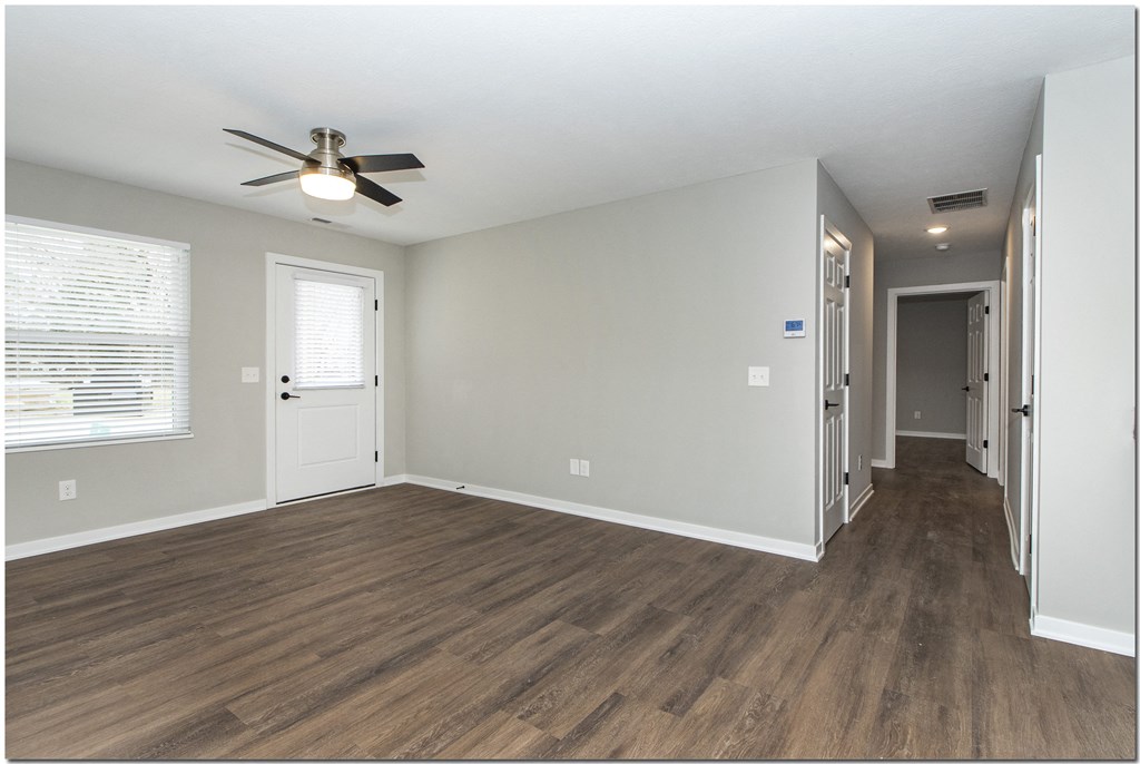 an empty living room with a ceiling fan and a door to a hallway