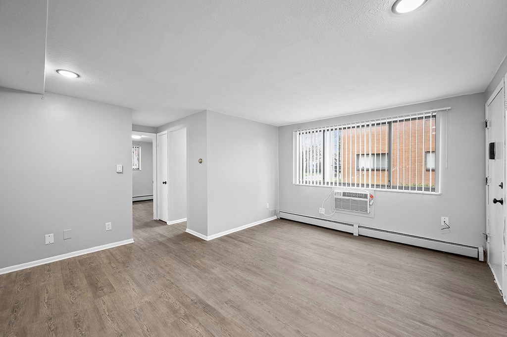 the living room and dining room of an apartment with white walls and wood flooring