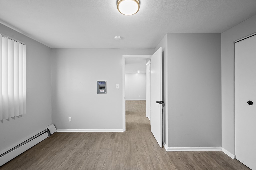 an empty room with white walls and wood flooring and a hallway with a door
