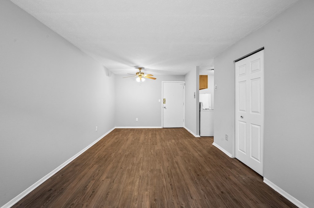 a spacious living room with white walls and wood flooring and a ceiling fan