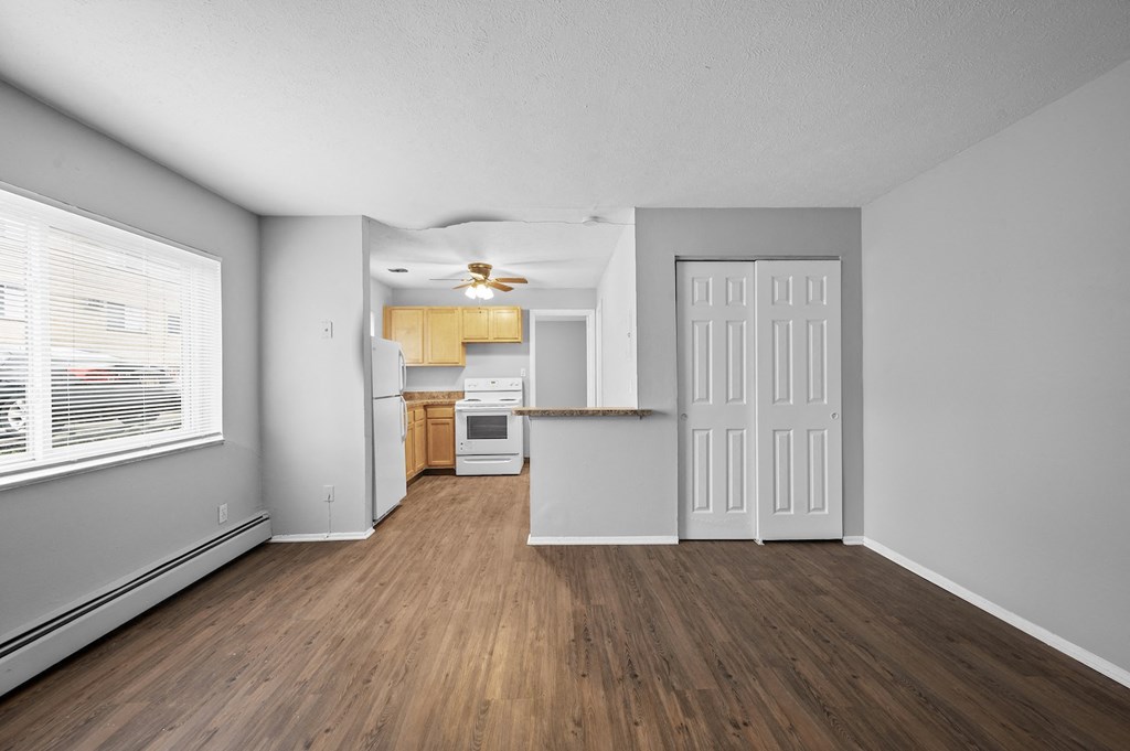 the living room and kitchen of an apartment with wood flooring and a large window