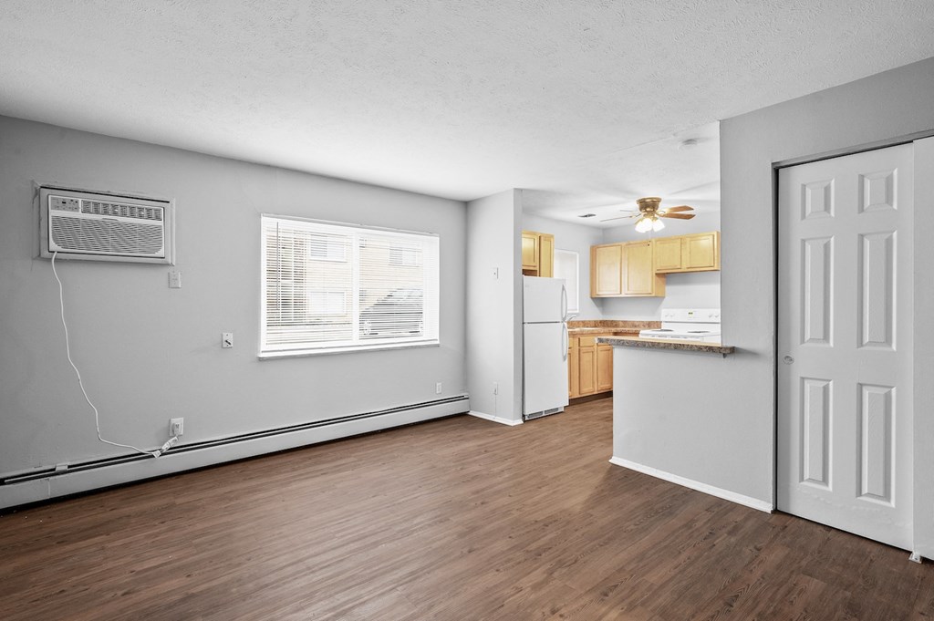 the living room and kitchen of an apartment with wood flooring and white walls
