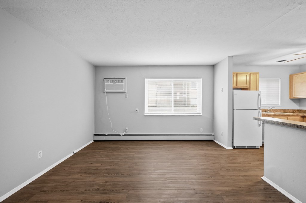 the living room and kitchen of an apartment with wood flooring and white walls