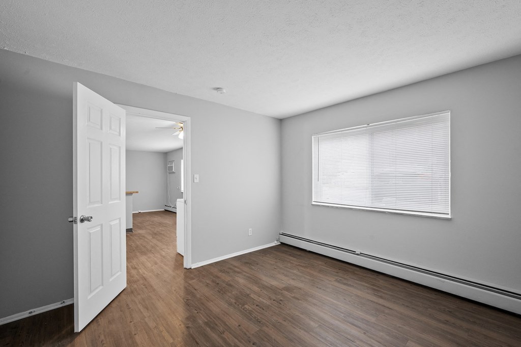 the living room and dining room of an apartment with wood flooring and a window