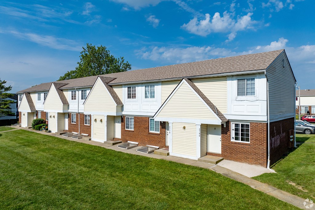 a row of white houses with a green lawn and a blue sky