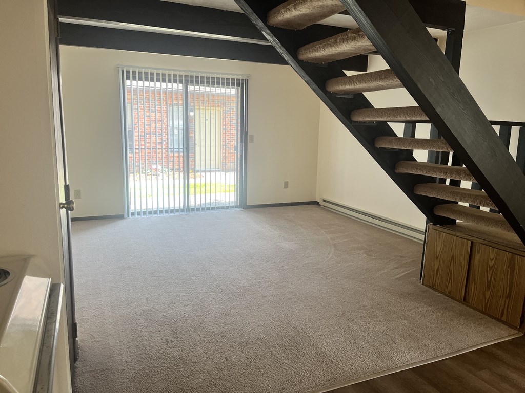 A carpeted room with a staircase leading to the upper floor.