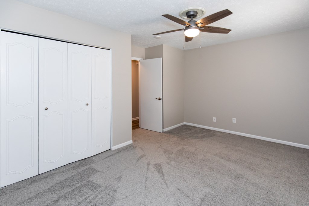 an empty living room with a ceiling fan and white closets
