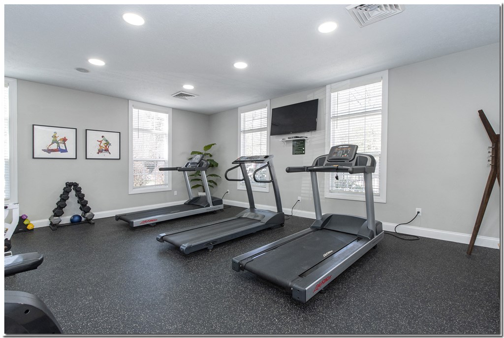a gym with three treadmills and a flat screen tv