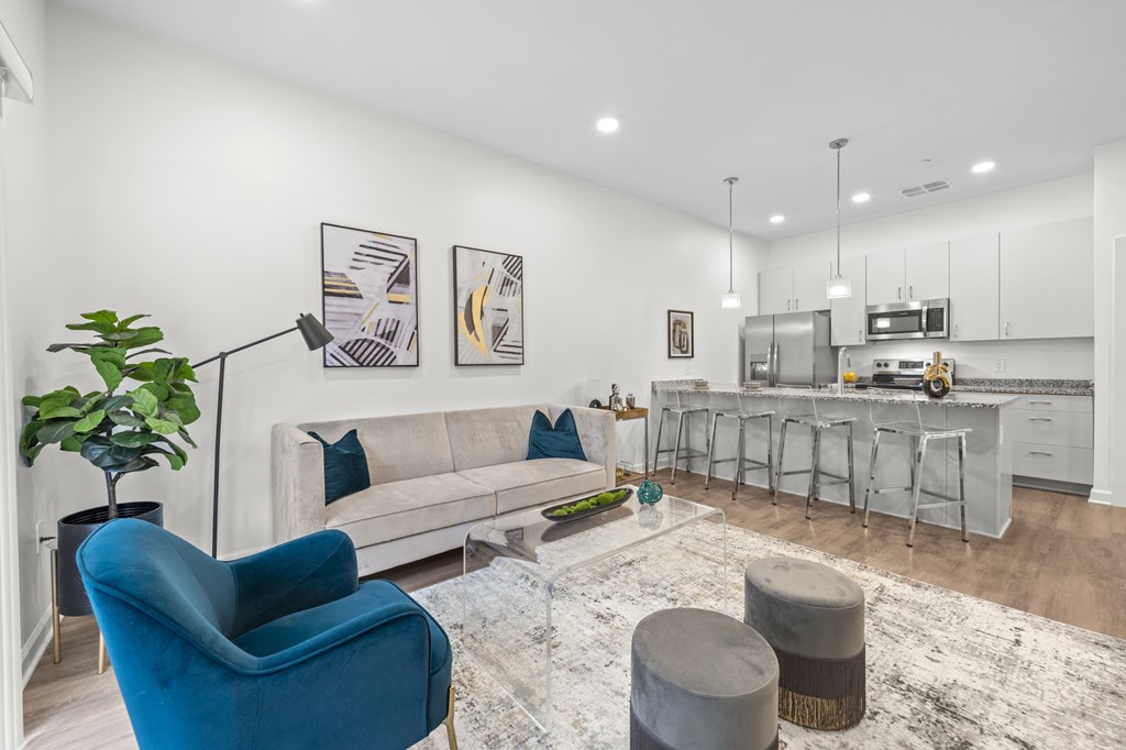 A blue armchair sits in a living room with a white couch and a rug. at The Lumos Apartments, Cleveland, Ohio