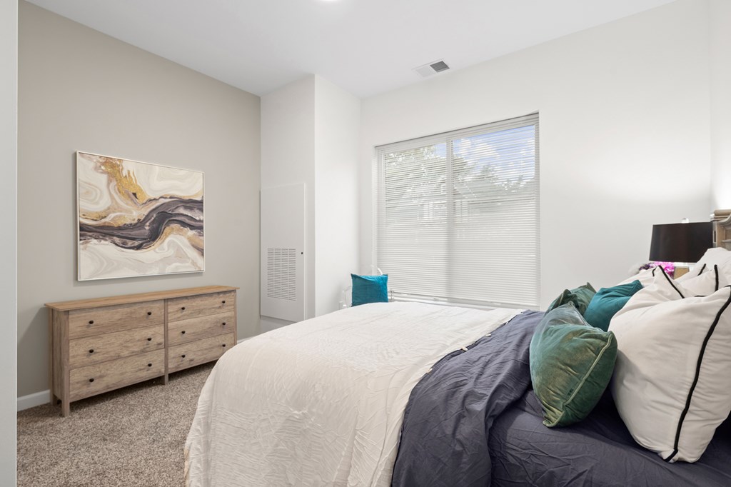 A bedroom with a bed, dresser, and a painting on the wall. at The Lumos Apartments, Cleveland, OH, 44106