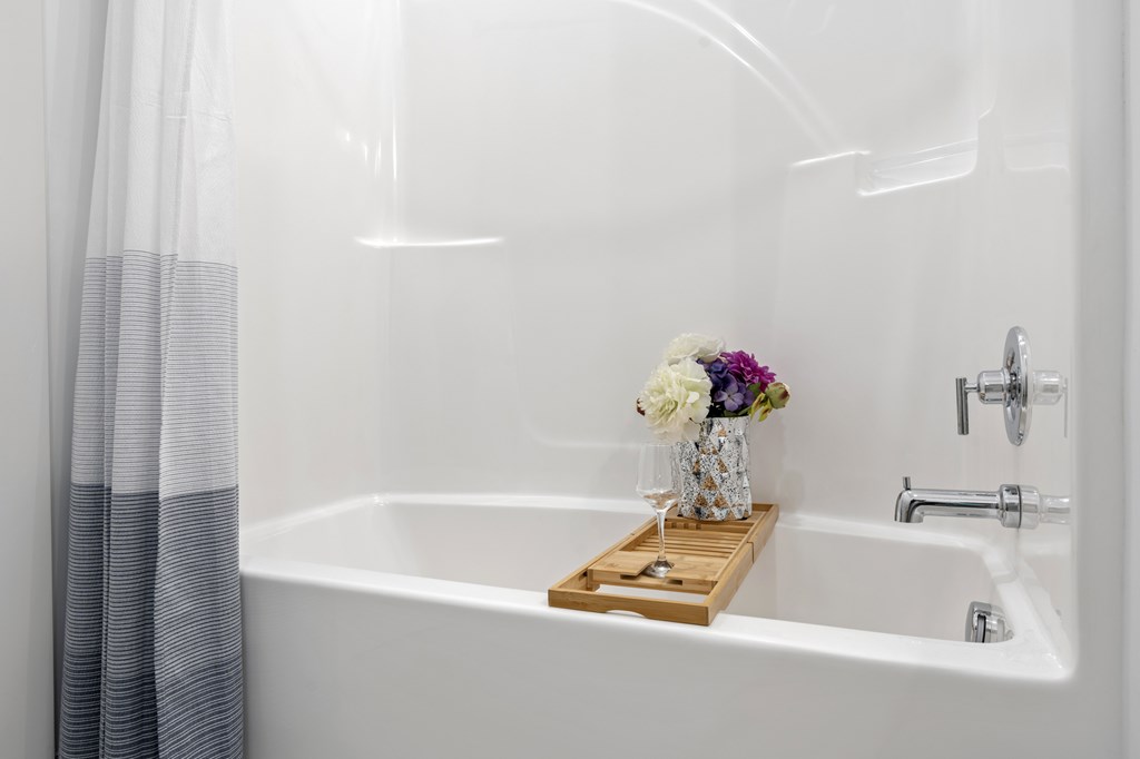A white bathtub with a wooden tray holding a vase of flowers. at The Lumos Apartments, Cleveland, Ohio