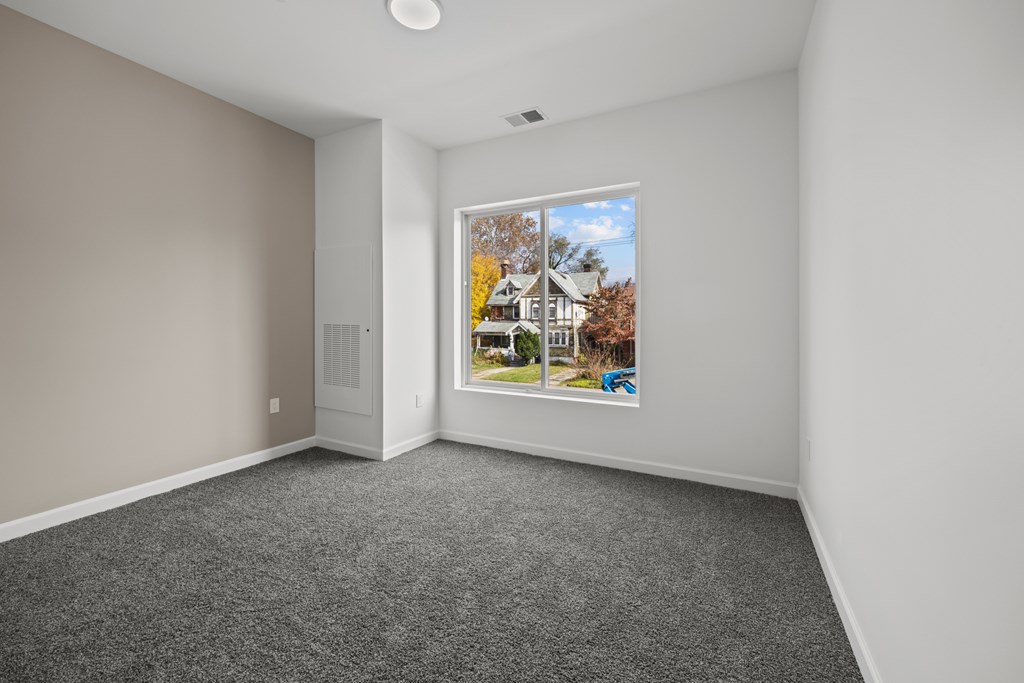 A room with a grey carpet and a picture of a house on the wall. at The Lumos Apartments, Cleveland, OH, 44106