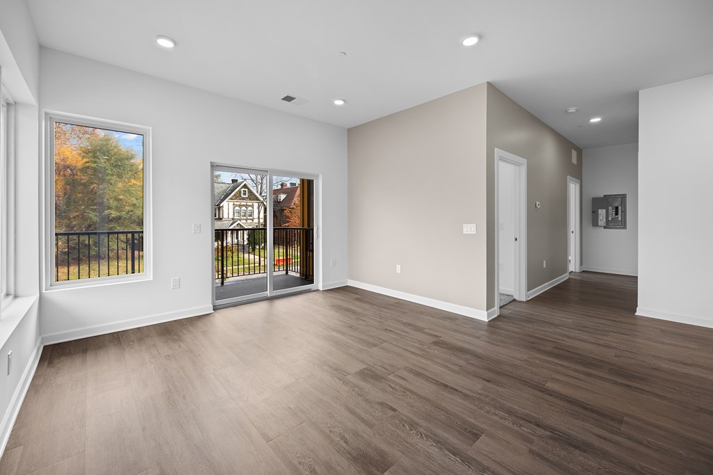 A spacious room with wooden flooring and a view of a house through a glass door. at The Lumos Apartments, Cleveland, Ohio