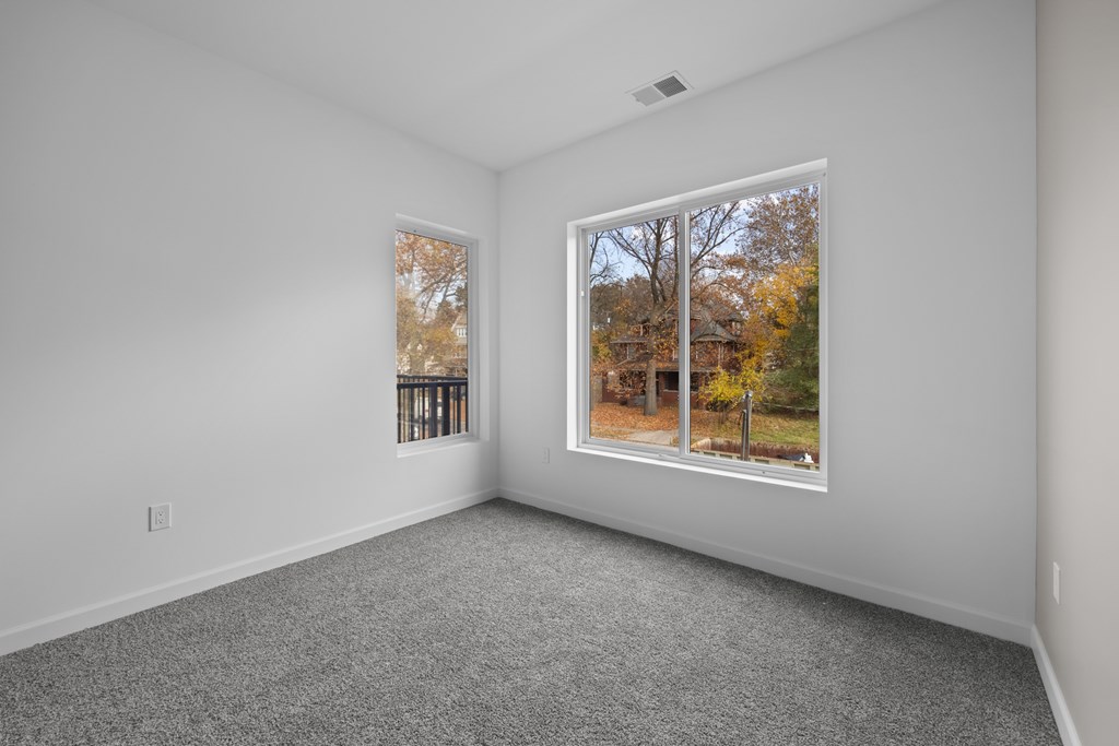 A room with a grey carpet and a window showing a tree with yellow leaves. at The Lumos Apartments, Cleveland, OH
