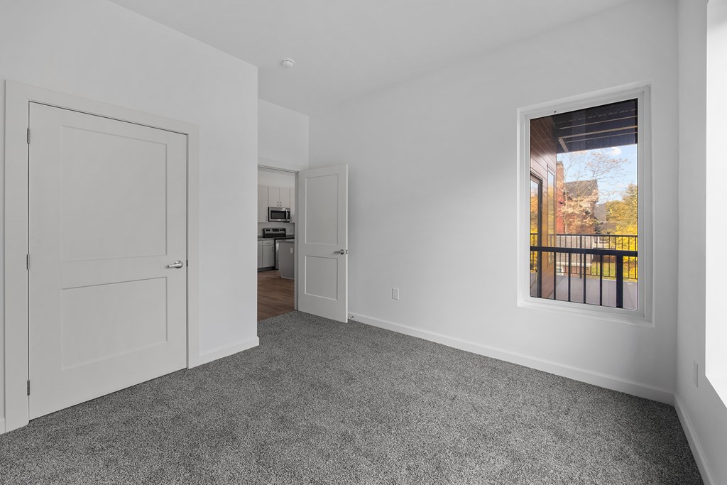A room with a grey carpet and a window showing a balcony. at The Lumos Apartments, Ohio