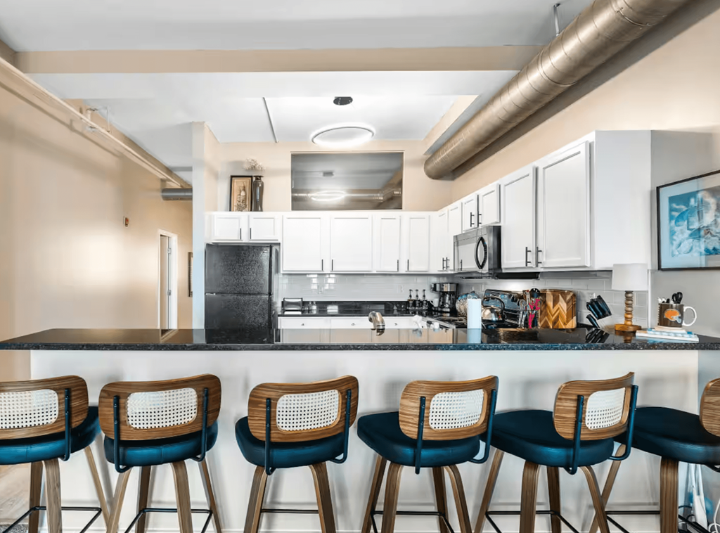 A kitchen with a bar area featuring a black counter and blue barstools.