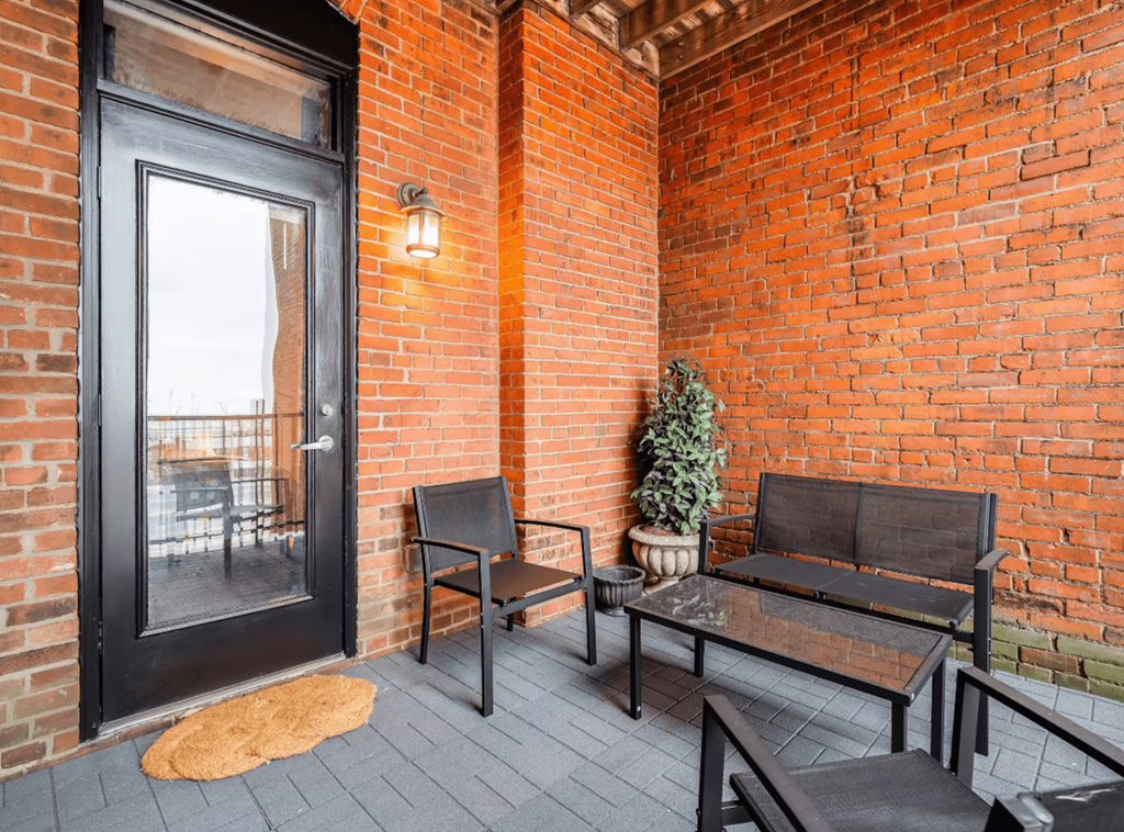 A black door is on the left of a brick wall with a bench and a table in front of it.