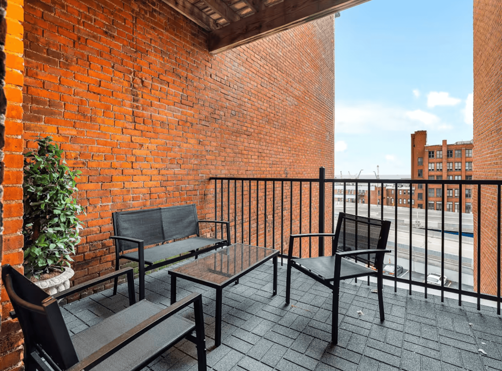 A balcony with a black metal railing and furniture including a couch, chair and table.