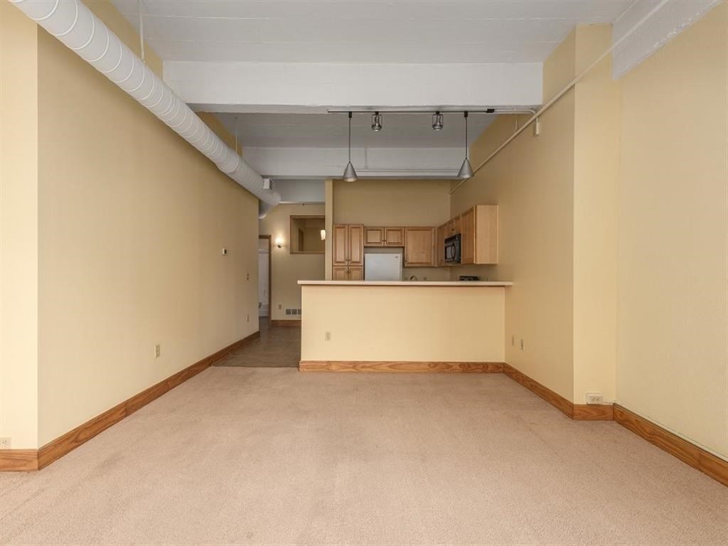 an empty living room with a kitchen in the background
