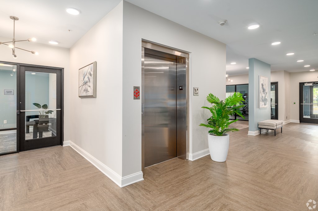 A modern office hallway with a wooden floor, a glass door, a potted plant, and a bench. at Park Lamont Townhomes Apartments, Cleveland, Ohio