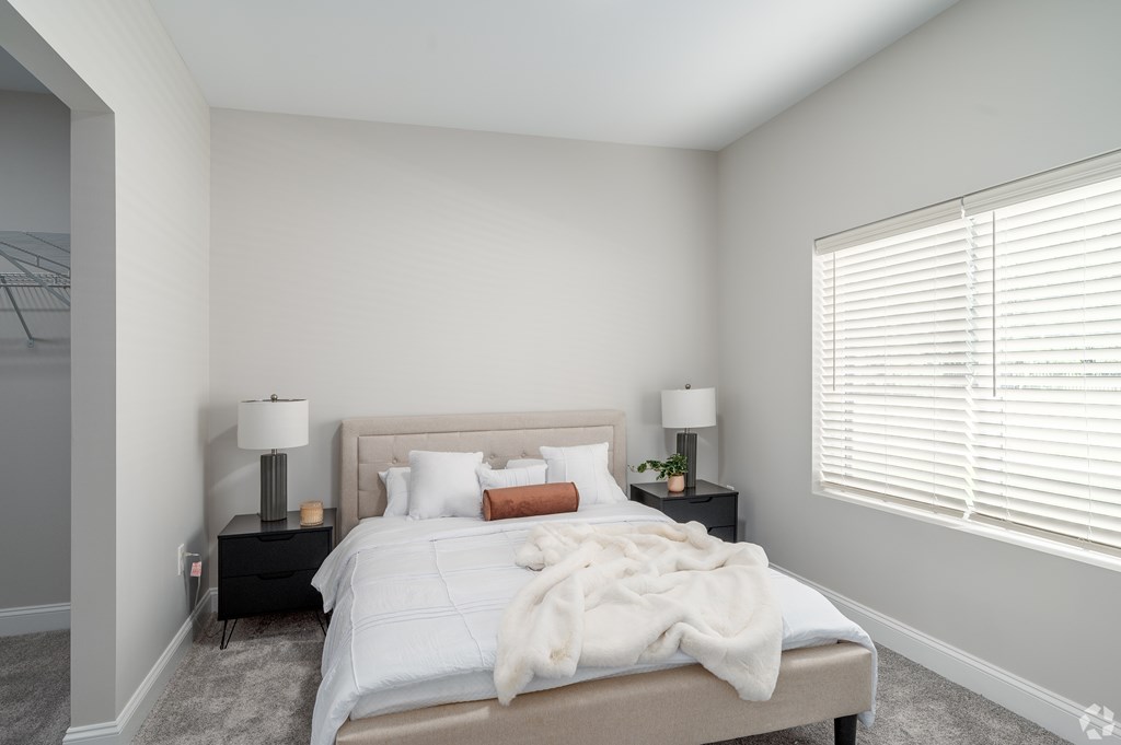 A bedroom with a bed, two lamps, and a window with blinds. at Park Lamont Townhomes Apartments, Cleveland, OH