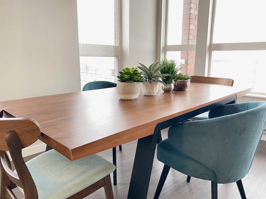 a wooden table with blue chairs and potted plants in a room with windows