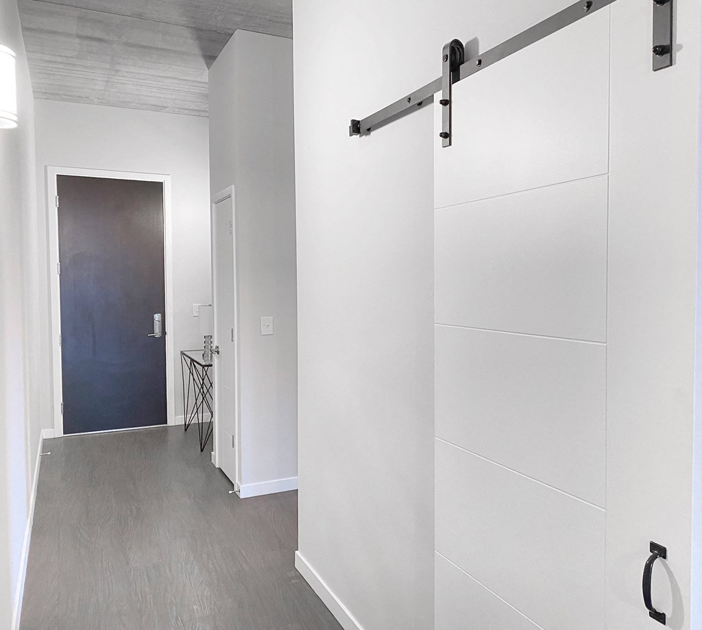 a white hallway with a black door and white closets and a wood floor