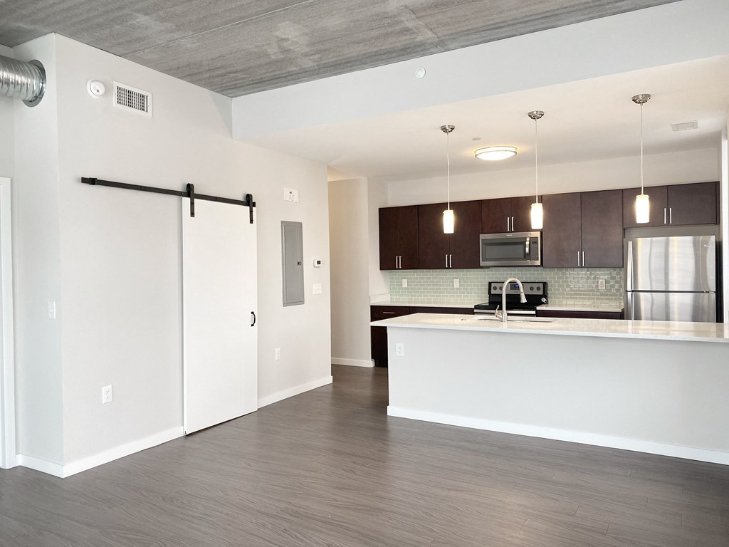 an empty living room with a kitchen with a refrigerator and a sink