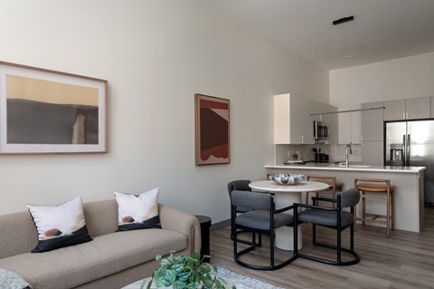 A living room with a grey couch and a dining table with chairs.