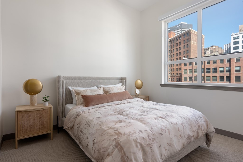 A bedroom with a large bed and a window overlooking a cityscape.