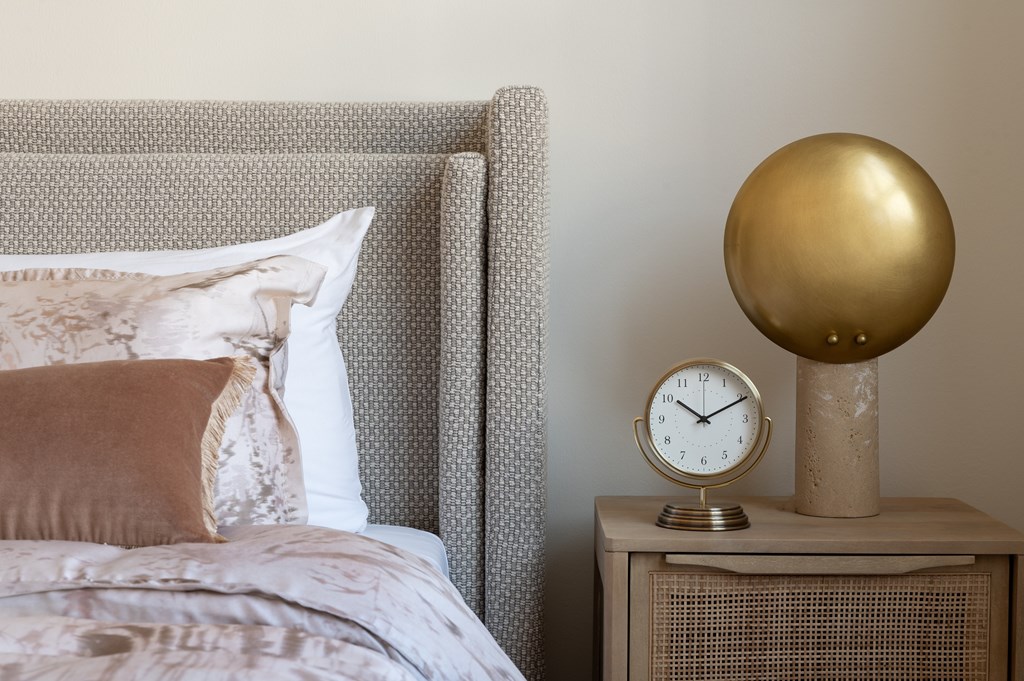 A bed with a pillow and a clock on a side table.