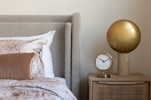 A bed with a pillow and a clock on a side table.