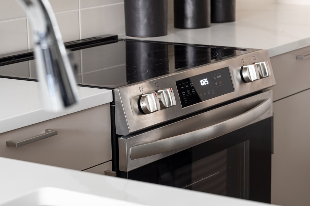 A modern stainless steel oven with a digital display and control knobs is installed in a kitchen.