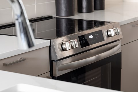 A modern stainless steel oven with a digital display and control knobs is installed in a kitchen.