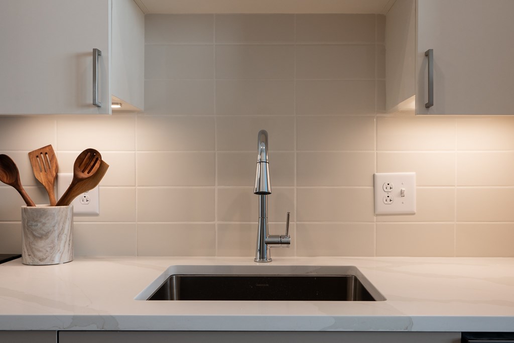 A kitchen sink with a faucet and a holder with wooden utensils.