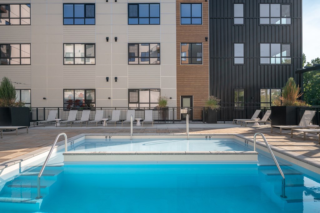 A swimming pool in front of a building with lounge chairs around it.