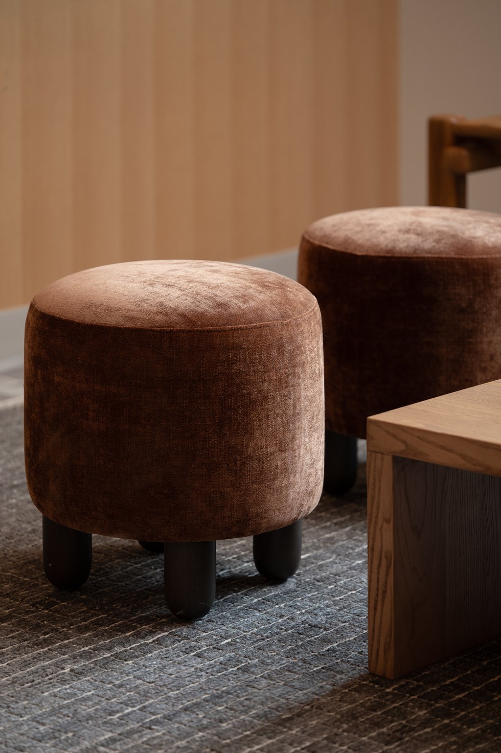 Two brown stools with black legs are placed on a grey carpet.