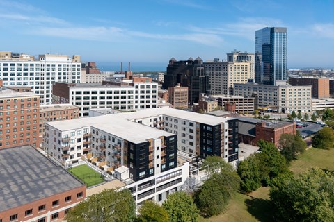 A cityscape with a mix of modern and older buildings, a green space in the foreground, and a clear sky.