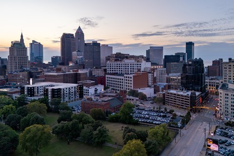 A cityscape with a mix of modern and older buildings, a parking lot, and trees in the foreground.