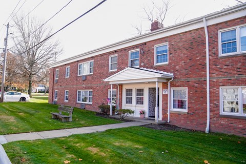 the front of a brick building with a sidewalk and grass