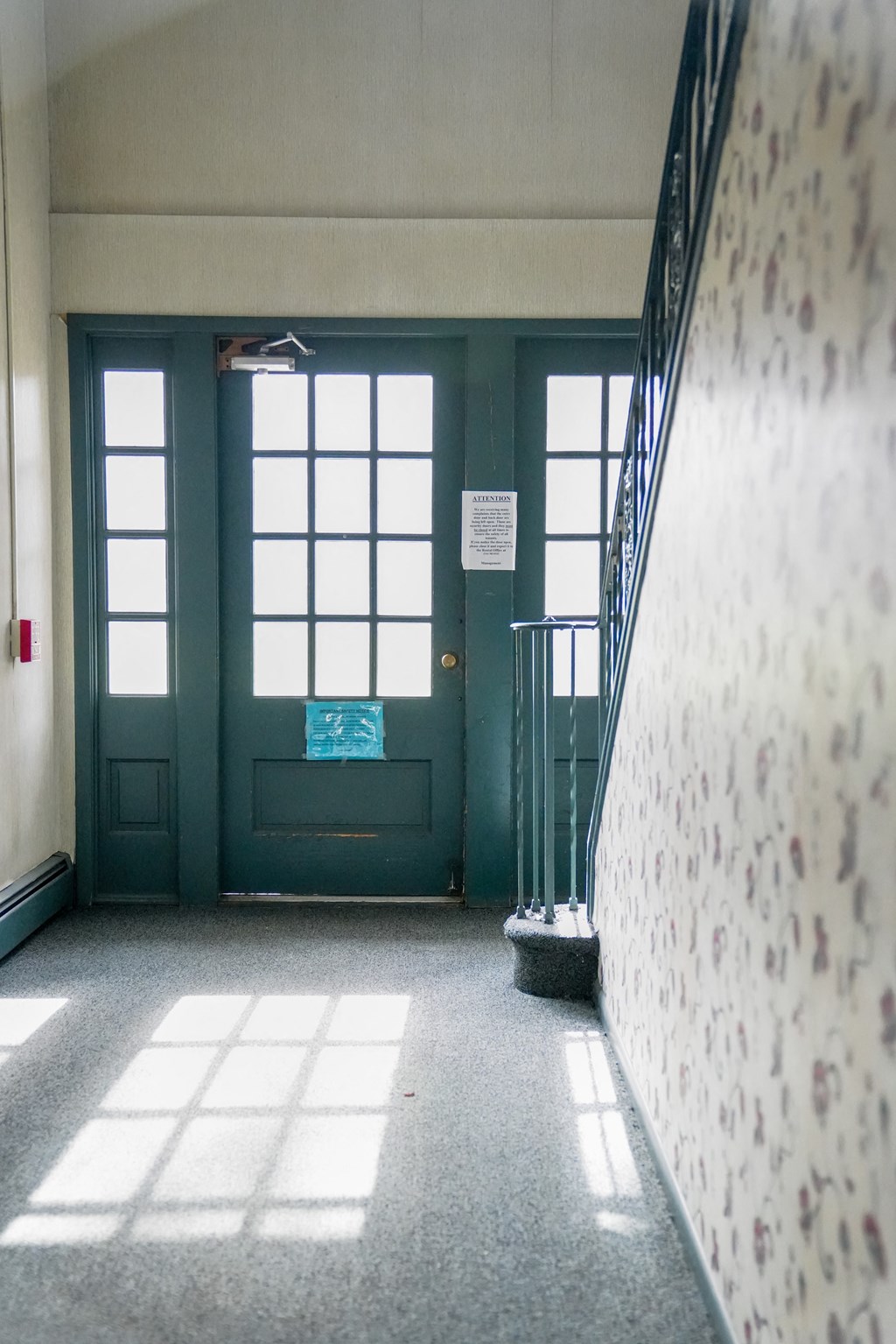 a hallway with stairs and a green door and windows